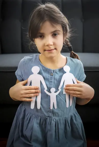 Young girl whose parents are going through a divorce holding a paper cut-out of a family whilst arguing over Residence and Contact for Children