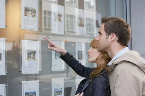 Couple viewing properties in an Estate Agents window whilst following the advice in Morgans Guide to Buying a House